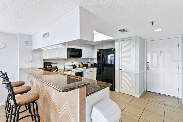 kitchen with a textured ceiling, a kitchen breakfast bar, black appliances, and white cabinetry