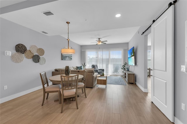 dining space with a barn door, ceiling fan, and light hardwood / wood-style flooring