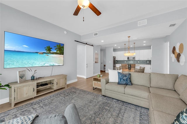 living room featuring a barn door, light hardwood / wood-style floors, and ceiling fan