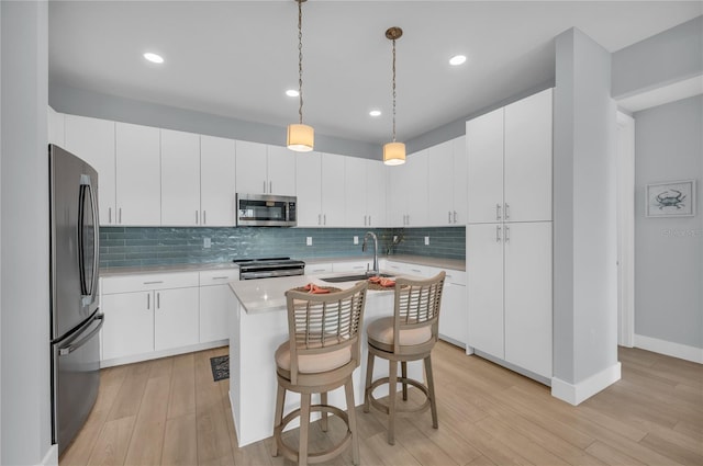 kitchen with appliances with stainless steel finishes, white cabinetry, light hardwood / wood-style flooring, and an island with sink