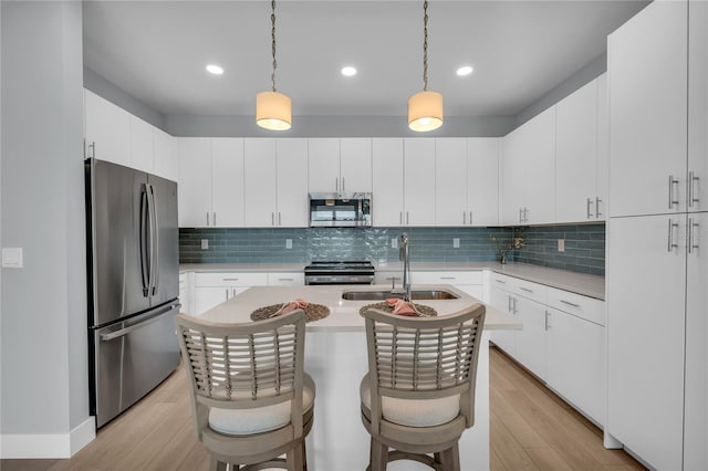 kitchen featuring an island with sink, stainless steel appliances, a breakfast bar, light hardwood / wood-style flooring, and white cabinets