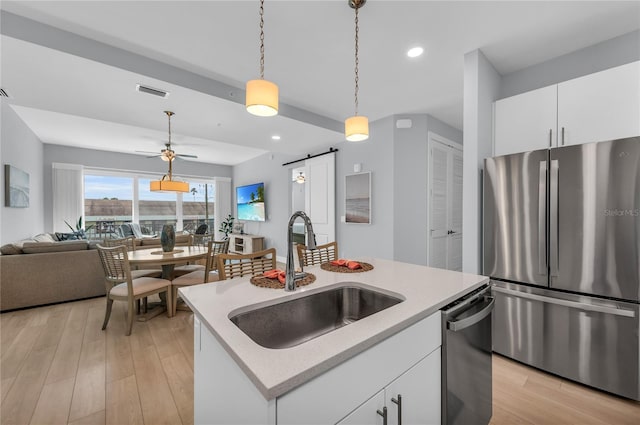 kitchen featuring sink, appliances with stainless steel finishes, light hardwood / wood-style floors, a barn door, and decorative light fixtures