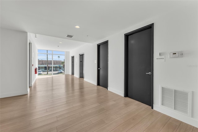 hallway featuring a wall of windows, light hardwood / wood-style flooring, and elevator