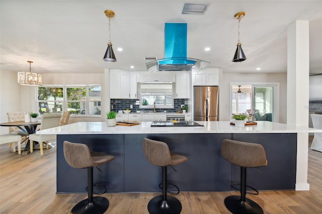 kitchen with island exhaust hood, stainless steel fridge, white cabinets, and hanging light fixtures