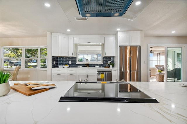 kitchen with appliances with stainless steel finishes, tasteful backsplash, light stone counters, sink, and white cabinets