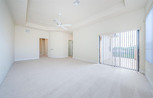 unfurnished room with ceiling fan, a tray ceiling, and light colored carpet