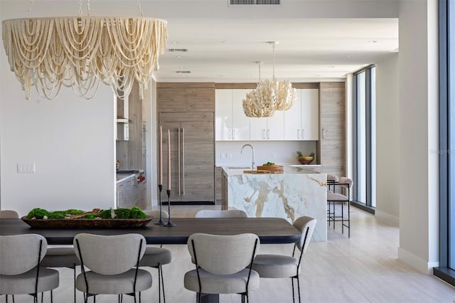 kitchen featuring an island with sink, stainless steel built in fridge, a notable chandelier, white cabinetry, and a breakfast bar area