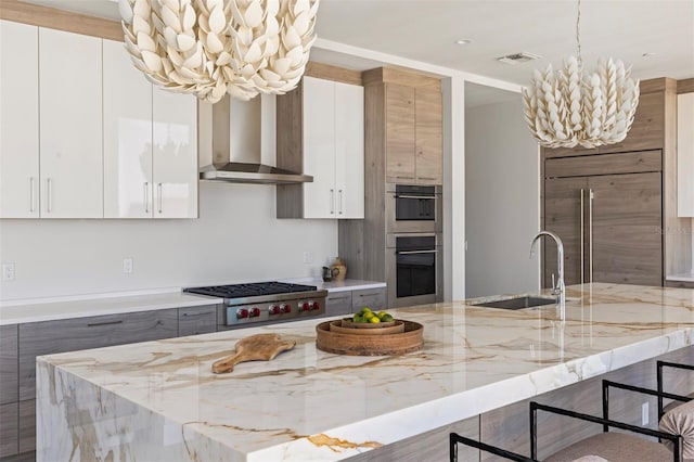 kitchen featuring appliances with stainless steel finishes, sink, wall chimney exhaust hood, and light stone counters