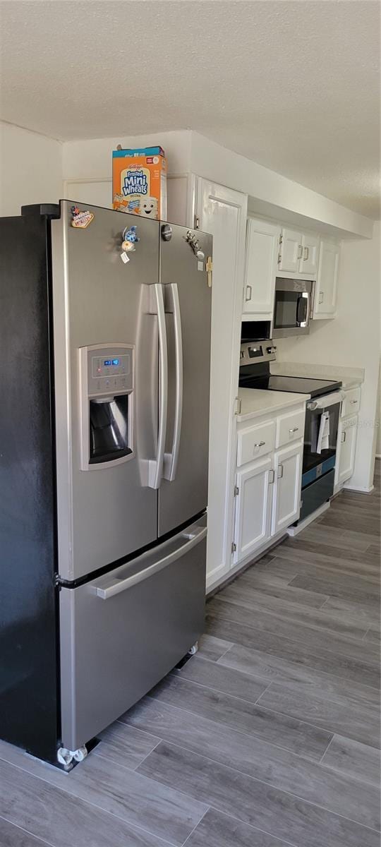 kitchen featuring stainless steel appliances, a textured ceiling, white cabinets, and light hardwood / wood-style floors