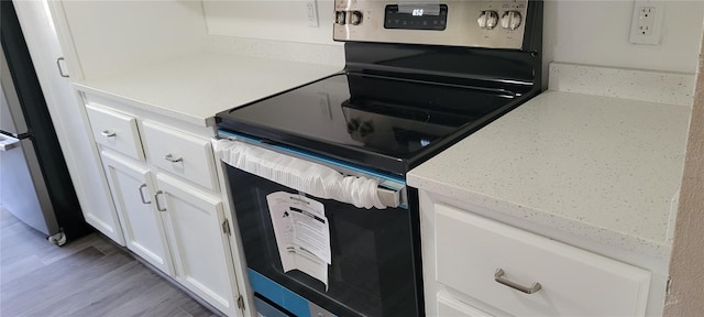 kitchen with refrigerator, stainless steel range with electric stovetop, hardwood / wood-style floors, light stone countertops, and white cabinets