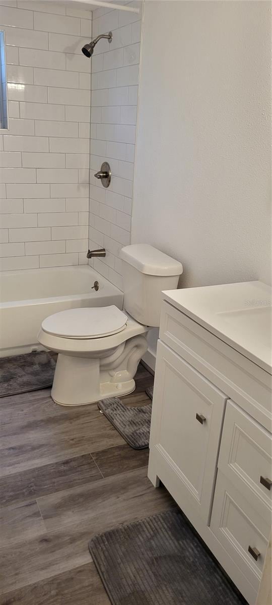 full bathroom featuring hardwood / wood-style flooring, tiled shower / bath, vanity, and toilet