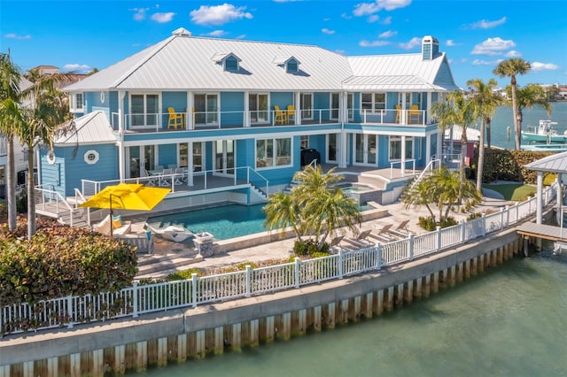 back of house featuring a swimming pool with hot tub, a balcony, a patio area, and a water view