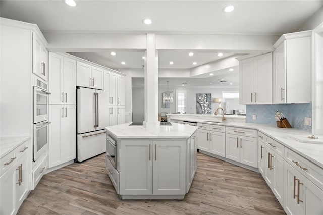 kitchen with kitchen peninsula, high end white fridge, sink, white cabinets, and a center island