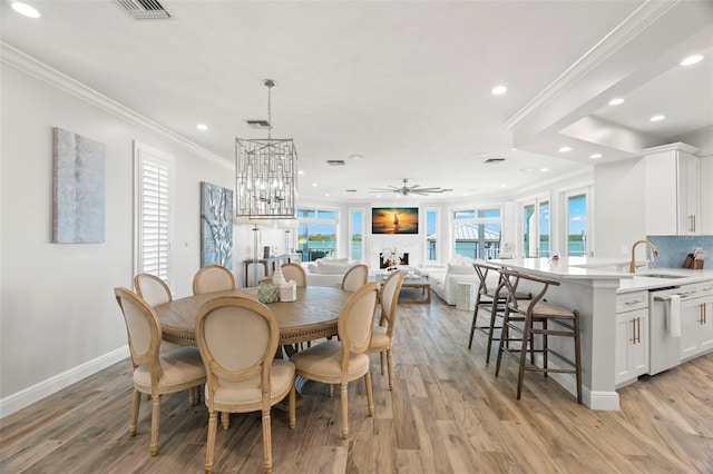 dining area featuring ceiling fan with notable chandelier, crown molding, light wood-type flooring, and sink