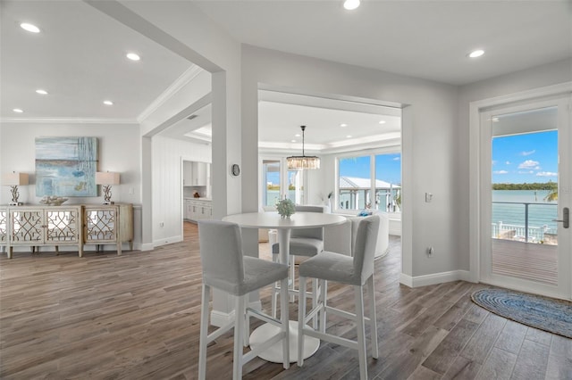 dining area featuring a water view, ornamental molding, dark wood-type flooring, and an inviting chandelier