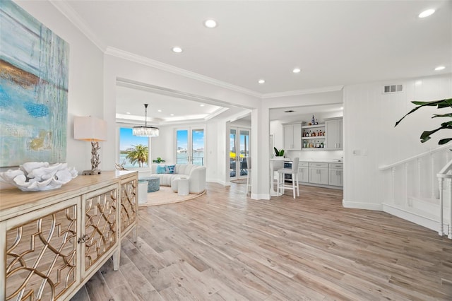 entrance foyer with bar area, crown molding, light hardwood / wood-style floors, and an inviting chandelier