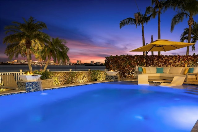 pool at dusk with pool water feature and an outdoor living space