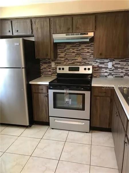 kitchen featuring tasteful backsplash, dark brown cabinetry, light tile flooring, and stainless steel appliances