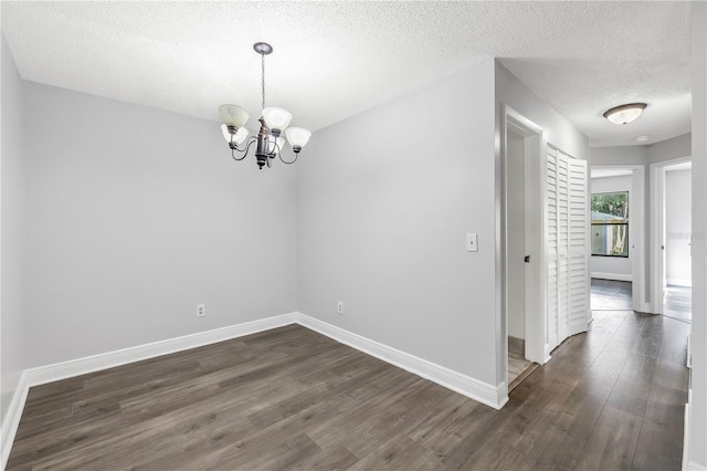 empty room featuring dark hardwood / wood-style floors, a textured ceiling, and a notable chandelier