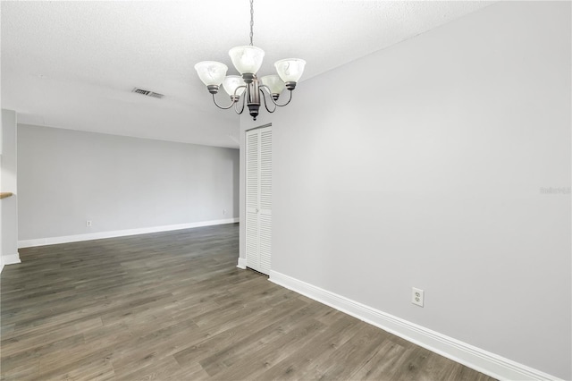 empty room with dark hardwood / wood-style floors, a textured ceiling, and a chandelier