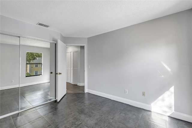 unfurnished bedroom featuring dark tile flooring, a textured ceiling, and a closet