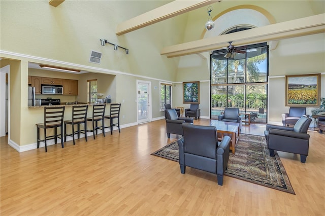 living room featuring light hardwood / wood-style flooring, ceiling fan, and a towering ceiling