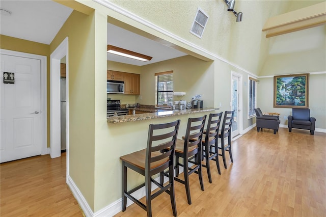 kitchen with electric range, stone countertops, a kitchen bar, light hardwood / wood-style floors, and a textured ceiling