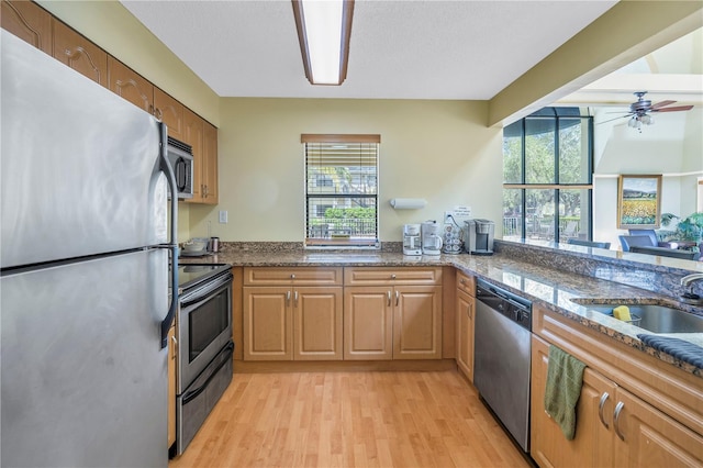 kitchen with ceiling fan, light hardwood / wood-style floors, sink, stainless steel appliances, and dark stone countertops