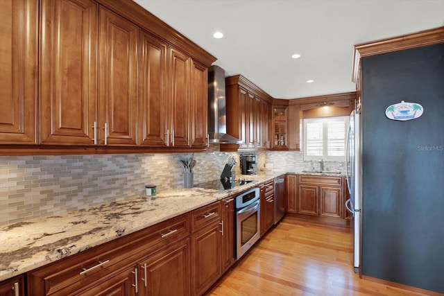 kitchen featuring light wood-type flooring, light stone counters, wall chimney exhaust hood, stainless steel appliances, and sink