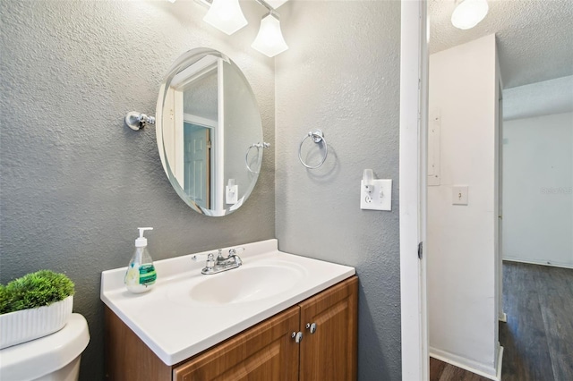 bathroom featuring wood-type flooring, toilet, a textured ceiling, and vanity