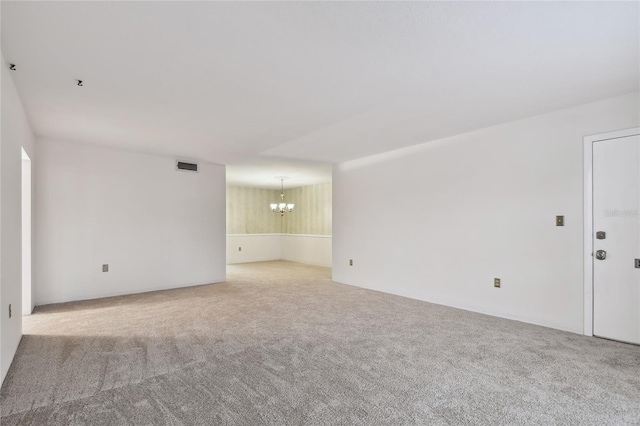 spare room featuring a chandelier and light colored carpet