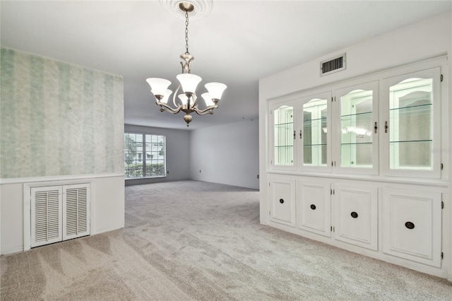 spare room with light colored carpet and an inviting chandelier