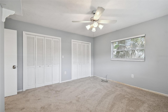 unfurnished bedroom with ceiling fan, multiple closets, and light carpet