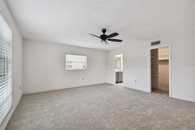 unfurnished bedroom with ceiling fan, light carpet, a walk in closet, connected bathroom, and a closet