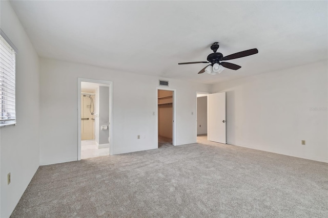 unfurnished bedroom with light carpet, a walk in closet, a closet, and ceiling fan