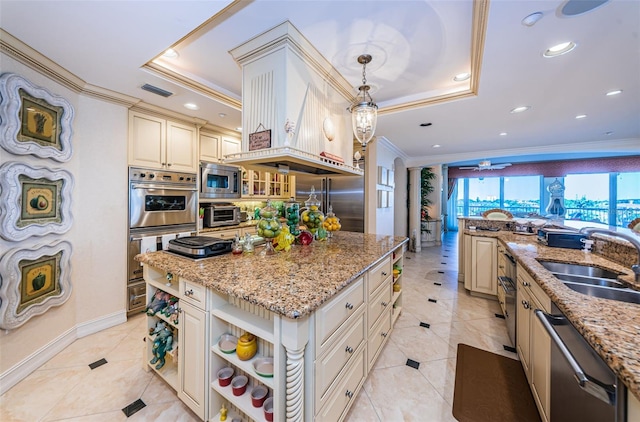 kitchen featuring a raised ceiling, stainless steel appliances, cream cabinets, and pendant lighting