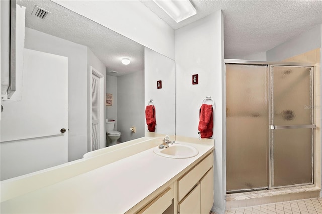 bathroom with tile flooring, a shower with shower door, large vanity, a textured ceiling, and toilet