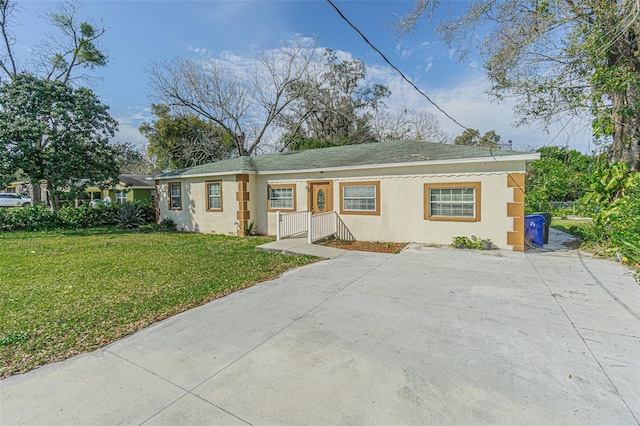ranch-style house featuring a front lawn, concrete driveway, and stucco siding