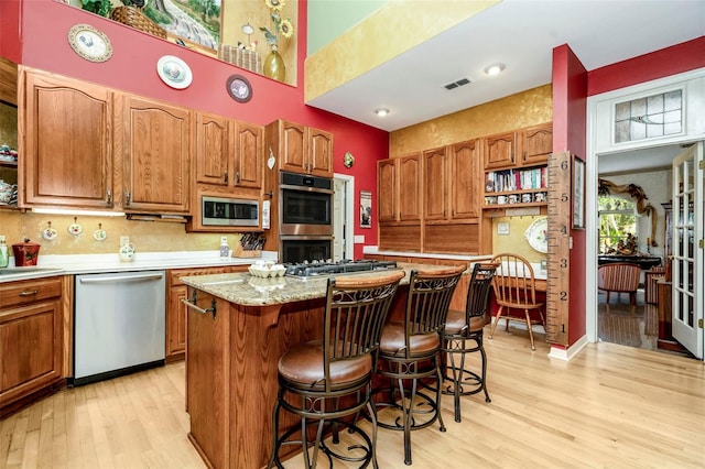 kitchen featuring a kitchen breakfast bar, light stone countertops, light wood-type flooring, a kitchen island, and stainless steel appliances