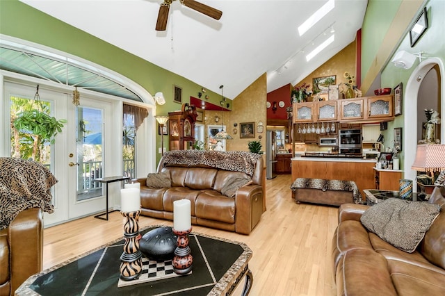 living room featuring light wood-type flooring, a skylight, high vaulted ceiling, and ceiling fan