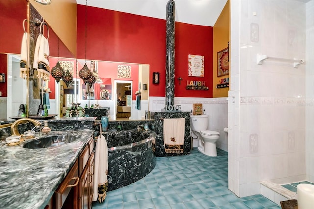 bathroom with a washtub, vanity, toilet, and tile walls