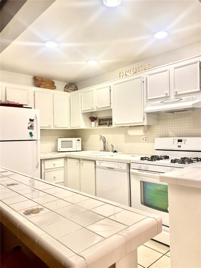 kitchen with light tile floors, tile counters, white appliances, and white cabinetry