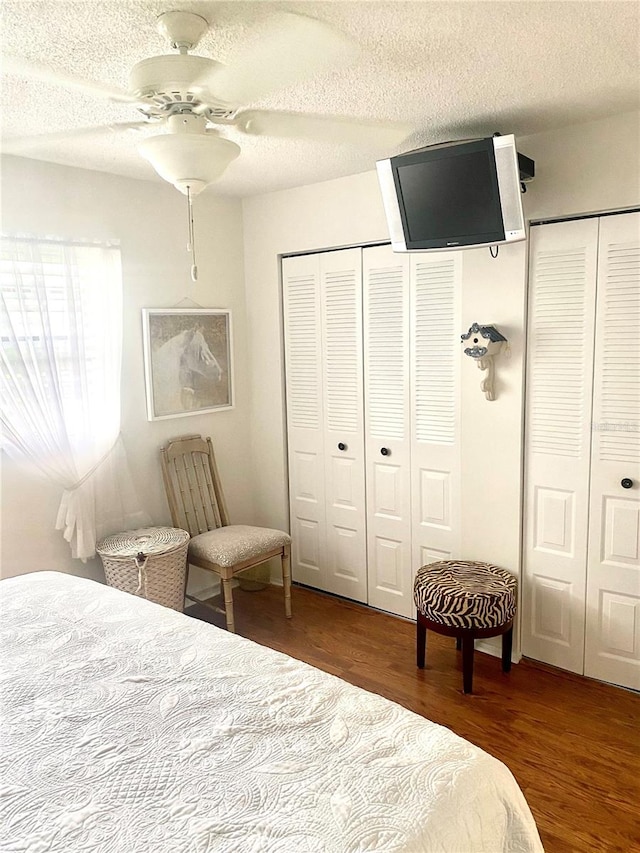 bedroom featuring ceiling fan, multiple closets, a textured ceiling, and dark wood-type flooring