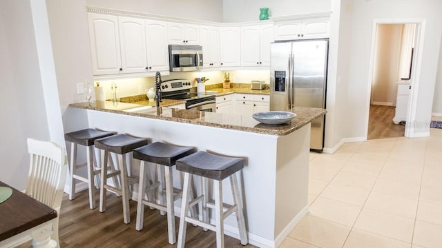 kitchen featuring dark stone countertops, kitchen peninsula, appliances with stainless steel finishes, and white cabinetry