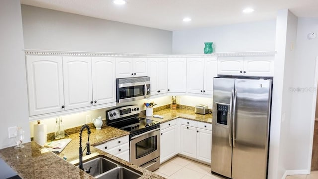 kitchen with dark stone countertops, stainless steel appliances, light tile floors, and white cabinetry