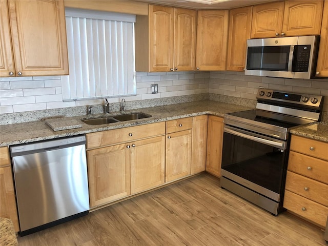 kitchen with stainless steel appliances, stone counters, a sink, and light wood-style flooring