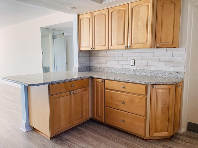 kitchen featuring a peninsula, light stone countertops, and wood finished floors