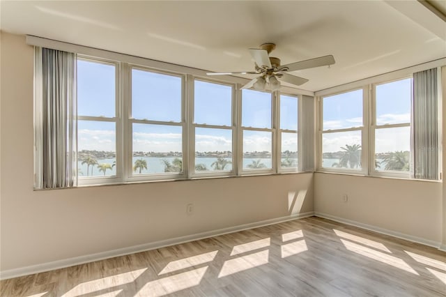 unfurnished sunroom with a water view, a ceiling fan, and a wealth of natural light