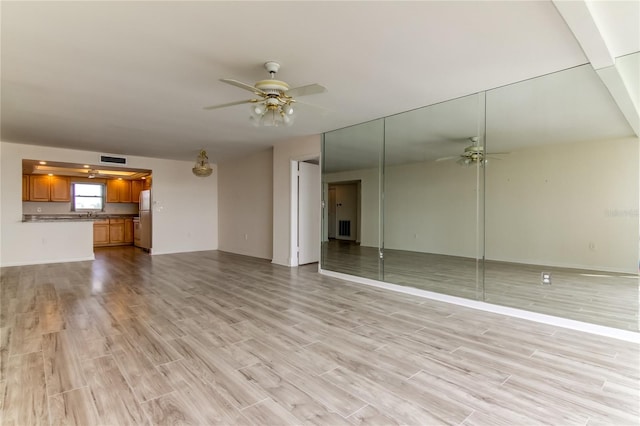 unfurnished living room featuring light wood-type flooring, ceiling fan, and sink