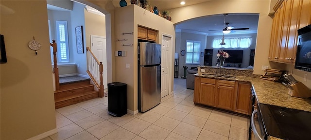 kitchen featuring sink, ceiling fan, crown molding, dark stone countertops, and stainless steel refrigerator